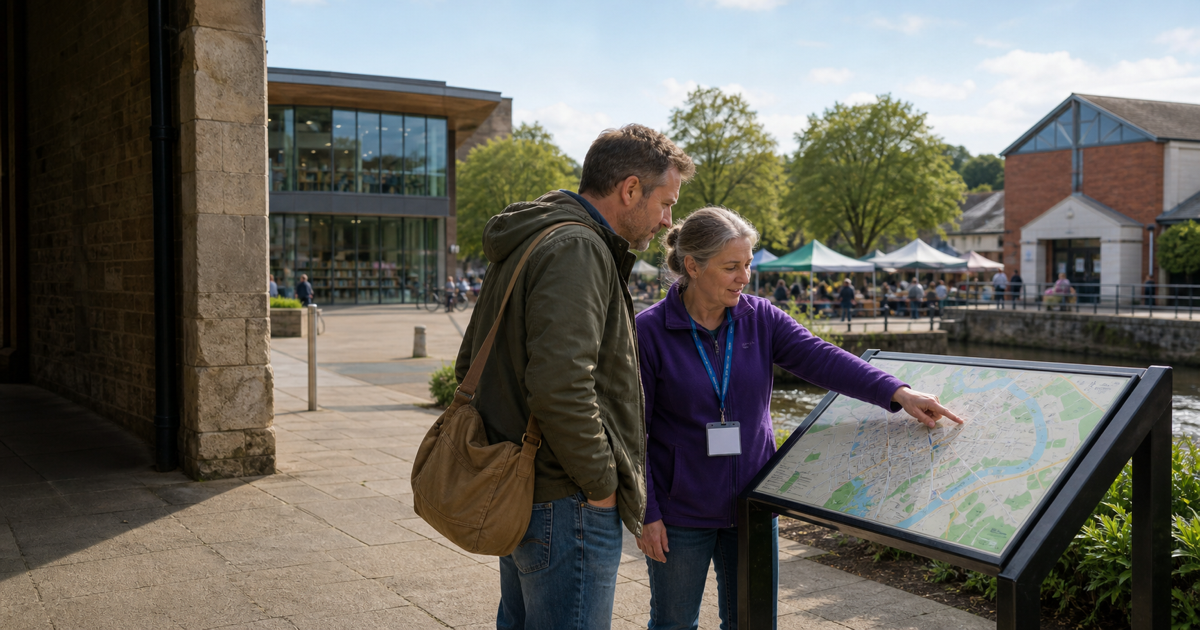 A local community volunteer guides a visitor using a public town map near a library and riverside market
